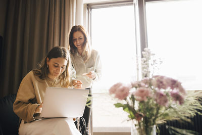 Smiling friends shopping online with credit card through laptop in hotel room