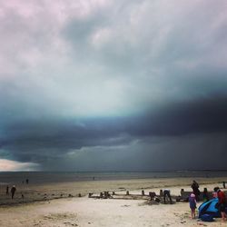 People on beach against cloudy sky
