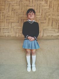Full length portrait of cute girl wearing school uniform standing against wall