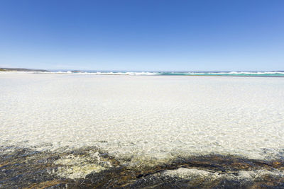 Surface level of beach against clear blue sky