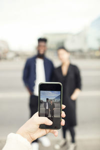 Cropped image of woman photographing friends in city