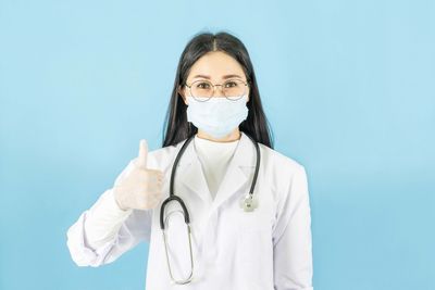 Portrait of doctor showing thumbs up against blue background