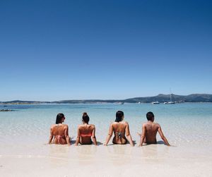 People at beach against clear blue sky