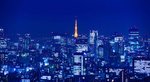 Illuminated buildings in city against blue sky