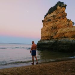 Full length of man standing on beach against sky during sunset
