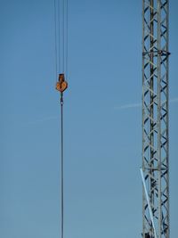 Low angle view of pulley hanging from crane against blue sky