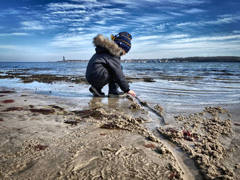 Side view of boy playing in sand on beach against sky