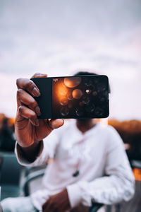 Midsection of person photographing with mobile phone against sky