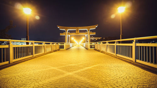 Illuminated street light on bridge against sky at night