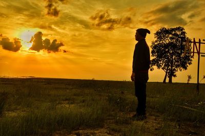 Man standing on field against sky during sunset
