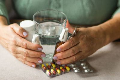 Woman's hands hold medicines throat and ear spray bottles, blisters of capsule, pill, glass of water