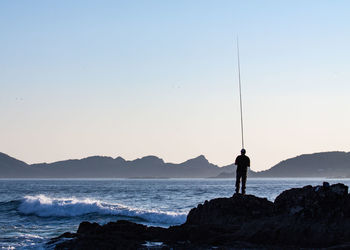 Man fishing at sea against clear sky