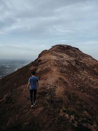 Rear view of man walking on mountain against sky