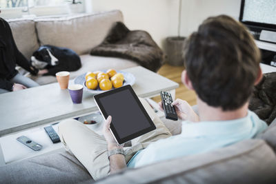 Man holding digital tablet while sitting on sofa at home