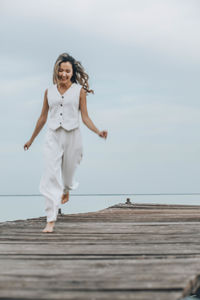 Portrait of young woman standing on pier over sea against sky