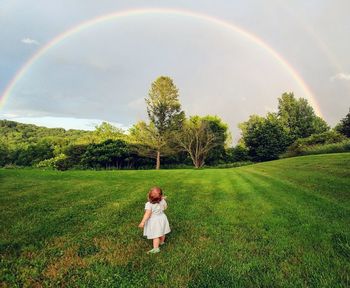 Full length of man standing on field against rainbow in sky