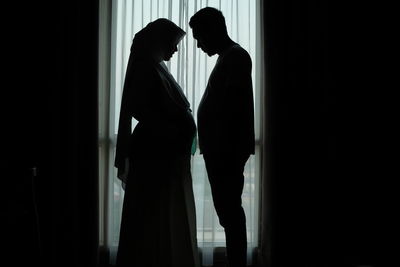 Side view of silhouette couple standing by window in darkroom