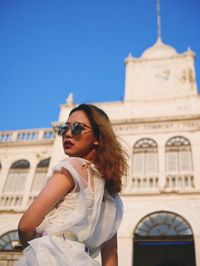 Portrait of young woman wearing sunglasses standing against built structure