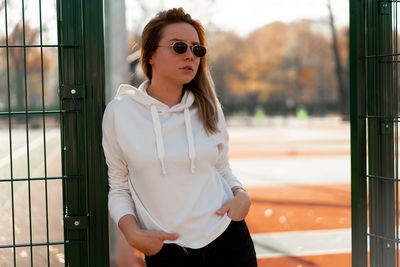 Young woman wearing sunglasses while standing against metal gate