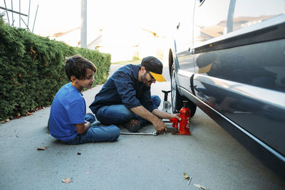 Father teaching son to use car jack while sitting at driveway