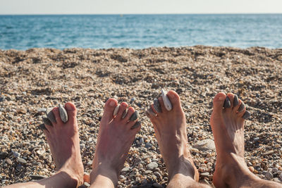 Low section of couple with pebbles sitting at beach