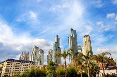 Low angle view of buildings and palm trees against sky at puerto madero