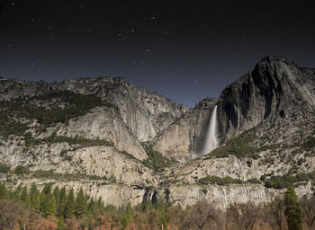 Low angle view of waterfall amidst rocky mountains against star field