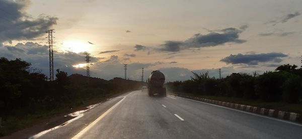 Road by trees against sky during sunset