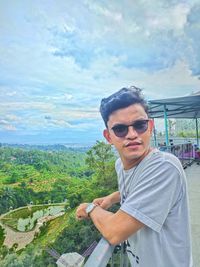 Young man wearing sunglasses standing against sky