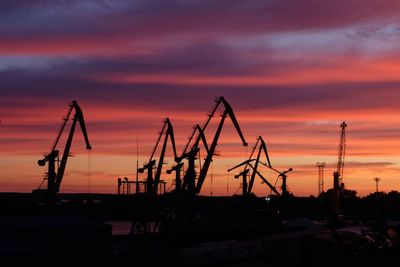 Silhouette cranes at construction site against sky during sunset