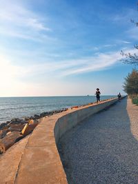 Mid distance view of girl running on promenade by sea against sky