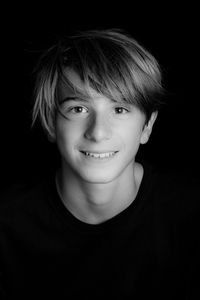 Close-up portrait of smiling teenage boy against black background