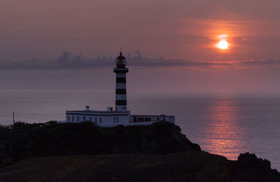 Lighthouse by sea against sky during sunset