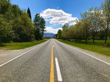 Empty road amidst trees against cloudy sky