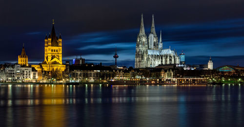 River against illuminated buildings and cologne cathedral in city at night