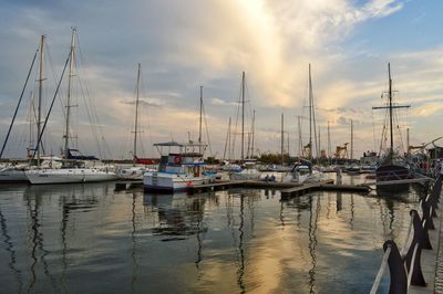 Sailboats moored at harbor against sky during sunset