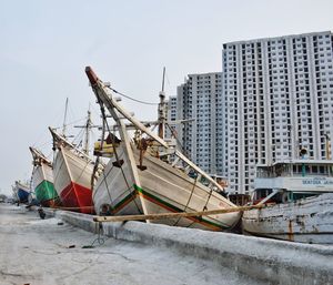 Fishing boats moored on shore against buildings in city