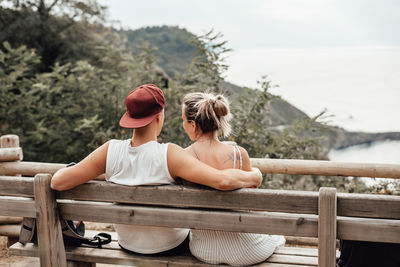 Rear view of young couple sitting on bench against sea