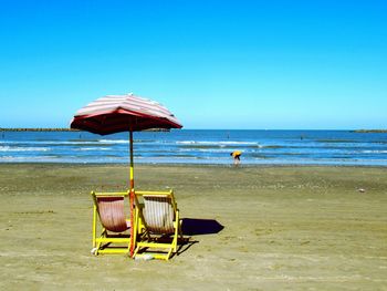 Deck chairs on beach against clear blue sky