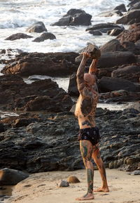 Shirtless man holding rock while standing at beach