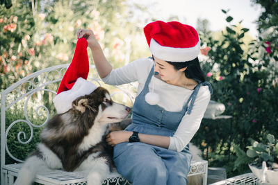 Smiling woman wearing santa hat with dog sitting outdoors