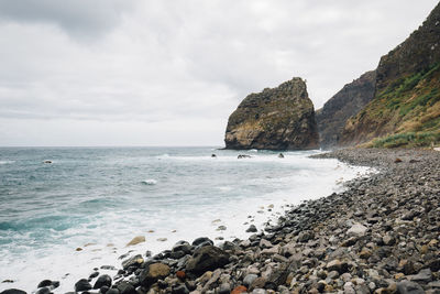 Scenic view of rock formation in sea against cloudy sky