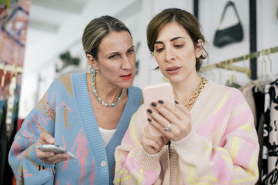 Female colleagues using smart phone in clothing store