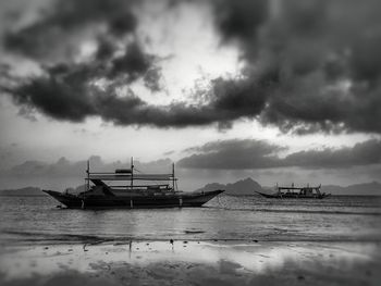 Boats moored in sea against cloudy sky