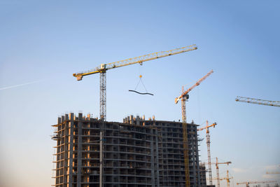 Low angle view of crane by building against clear blue sky