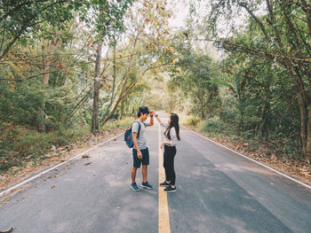 Rear view of couple walking on road along trees