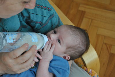 Mother feeding milk to toddler son while sitting on chair at home