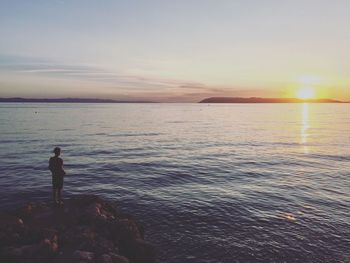 Man standing on rock formations by sea against sky during sunset