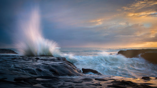 Sea waves splashing on shore against sky