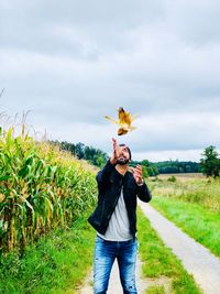 Man catching corn while standing at farm against cloudy sky